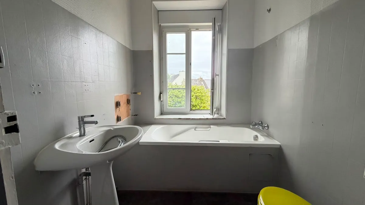 Ancienne salle de bain avec baignoire sous fenêtre et lavabo sur colonne