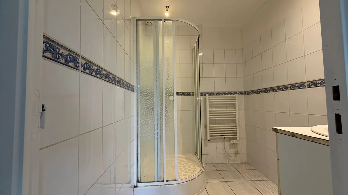 Ancienne salle de bain avec cabine de douche d'angle arrondie et carrelage blanc